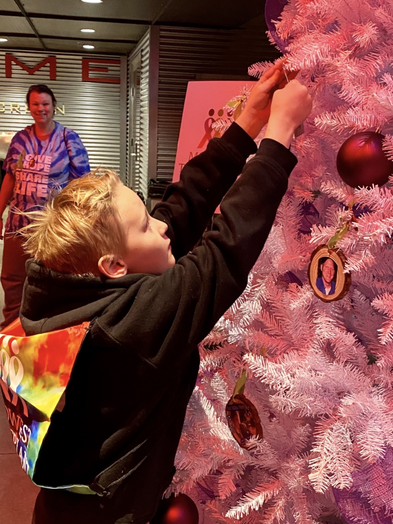 A child hanging something on a white holiday tree