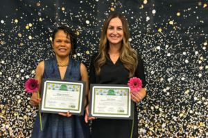 Two ladies holding certificates in front of a star-themed background.