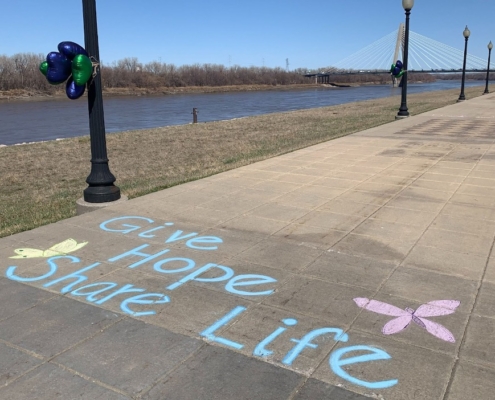 A photo of sidewalk chalk art with the Missouri River and Bond Bridge in the background.