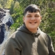 Photo image of Ryan Stoway in a hoodie with a waterfall and wooded scenery in the background.