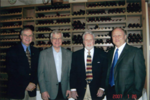 four people in suits in front of a wine rack