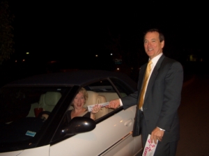 A person inside a car holding a pamphlet with a person standing outside the car