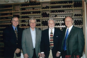 four people in suits standing in front of a wine rack