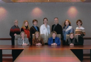 A group of people posing for a photo. Some are sitting behind of a desk and some are standing.