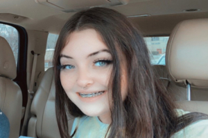 A photographic image of Chelsey Updike smiling into the camera while sitting in the driver's seat of a car.