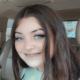 A photographic image of Chelsey Updike smiling into the camera while sitting in the driver's seat of a car.