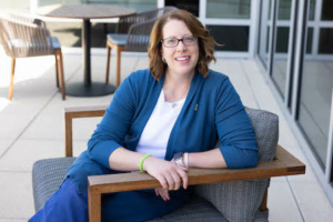 Portrait style photo of Julie Filbeck sitting in a low chair and smiling at the camera.