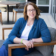 Portrait style photo of Julie Filbeck sitting in a low chair and smiling at the camera.