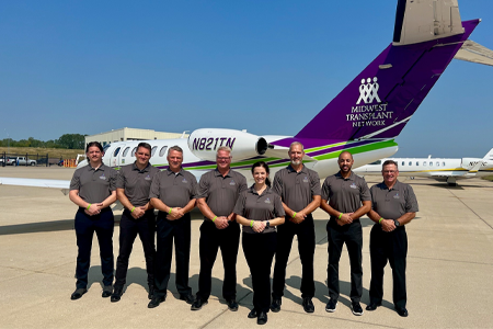 Pilots standing in formation in front of a plane owned by Midwest Transplant Network.