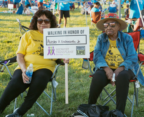 two people sitting in chairs holding a sign