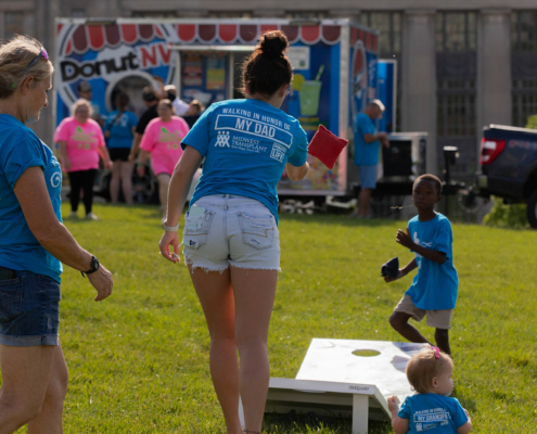 People playing cornhole on a grass field with a food truck in the background