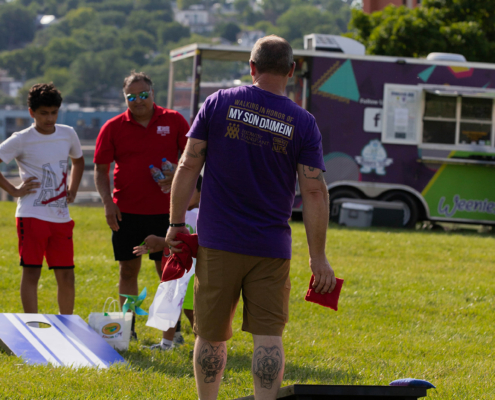 People playing cornhole on a grass field with a food truck in the background