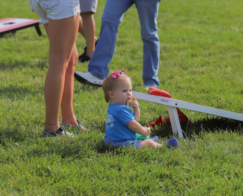 A child sitting on grass in front of a cornhole game