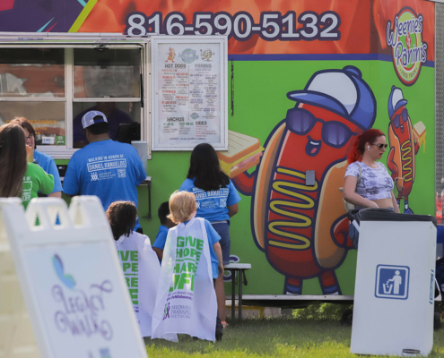 People infront of a food truck outside with a hot dog man character on the food truck