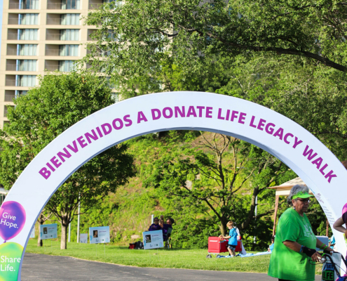 A sign over a path that says bienvenidos a donate life legacy walk