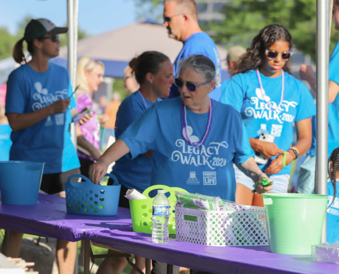 a table and people with Legacy Walk 2024 shirts standing behind it