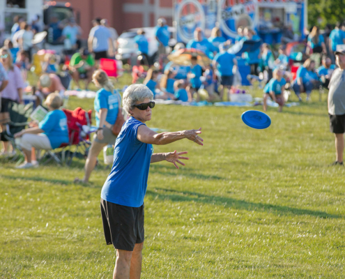 a person throwing a disc on a grass field with many people in the background