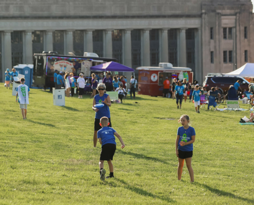 people on a grass field with food trucks and tents in the background