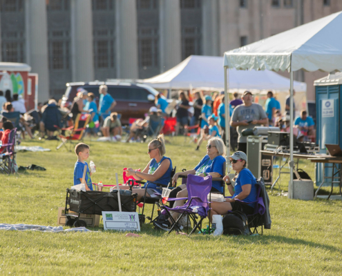 people sitting on a grass field with food trucks and tents in the background