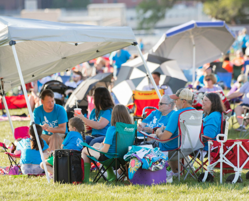 people sitting on a grass field outside with tents and umbrellas in the background