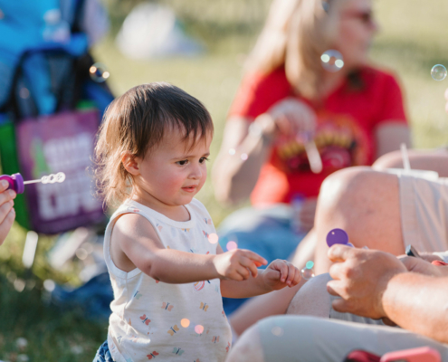 a child pointing at a bubble wand with bubbles in the background