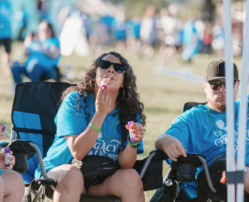 Two people sitting in chairs and one is blowing bubbles at an outdoor event