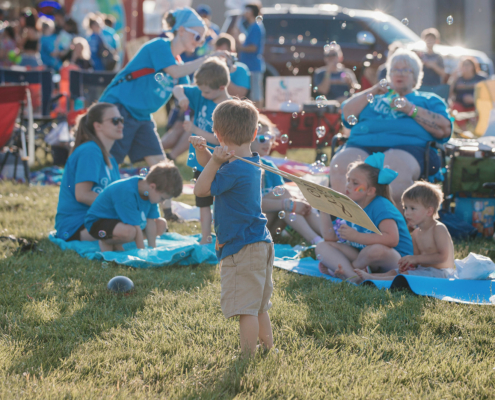 People sitting on chairs on a grass field. Some are blowing bubbles.