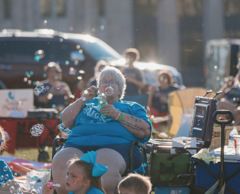 A person sitting in a chair and blowing bubbles at an outdoor event