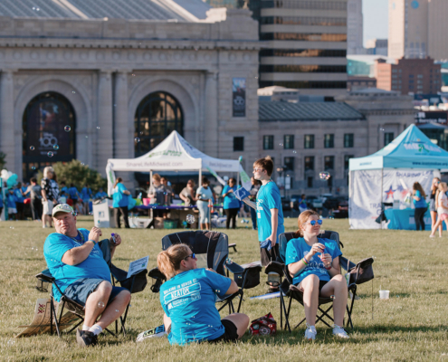 people sitting on chairs on a grass field with city buildings in the background