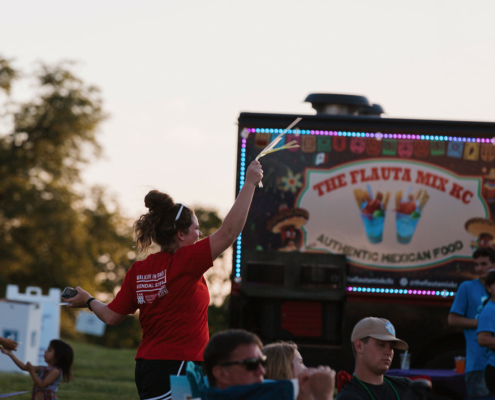 A person holding glow sticks with a food truck in the background