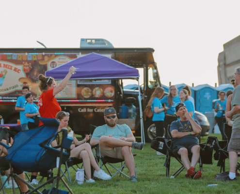 People standing and sitting in chairs next to a food truck