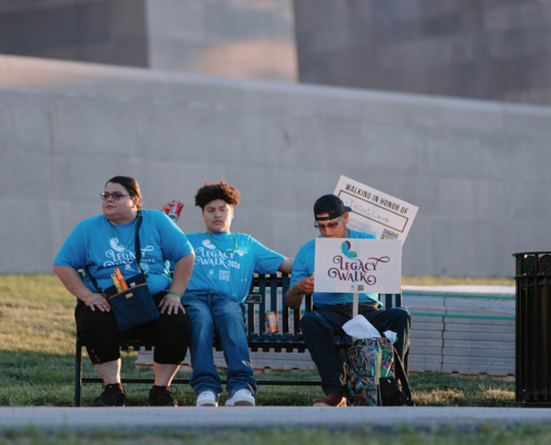 Three people sitting on a bench with a Legacy Walk sign