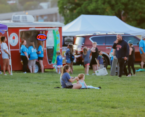 Children sitting on the grass with a food truck in the background.