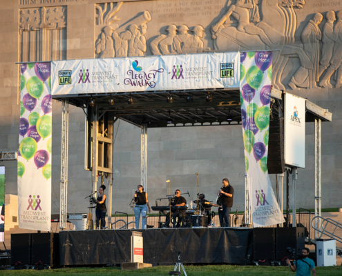 A stage setup with musicians performing under an event banner reading Legacy Walk.