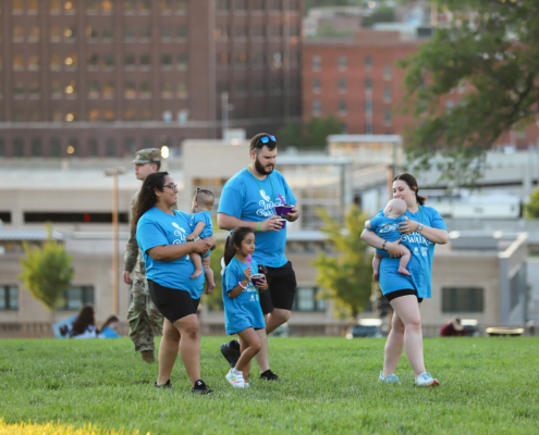 A group of people, walk across a grassy area in an urban park.