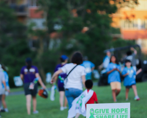 A group of people in a park, In the foreground, a sign reads "Give Hope, Share Life"