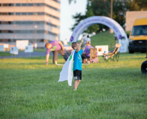 a child with their hands up wearing a cape on a grass field