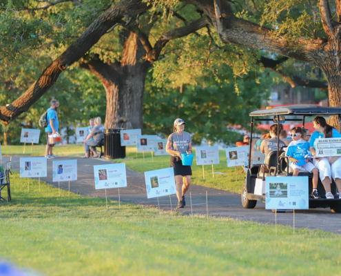 a person walking by a golf cart on a path with posters of donors along the path