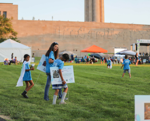 Adults and children walking with posters on a grass field